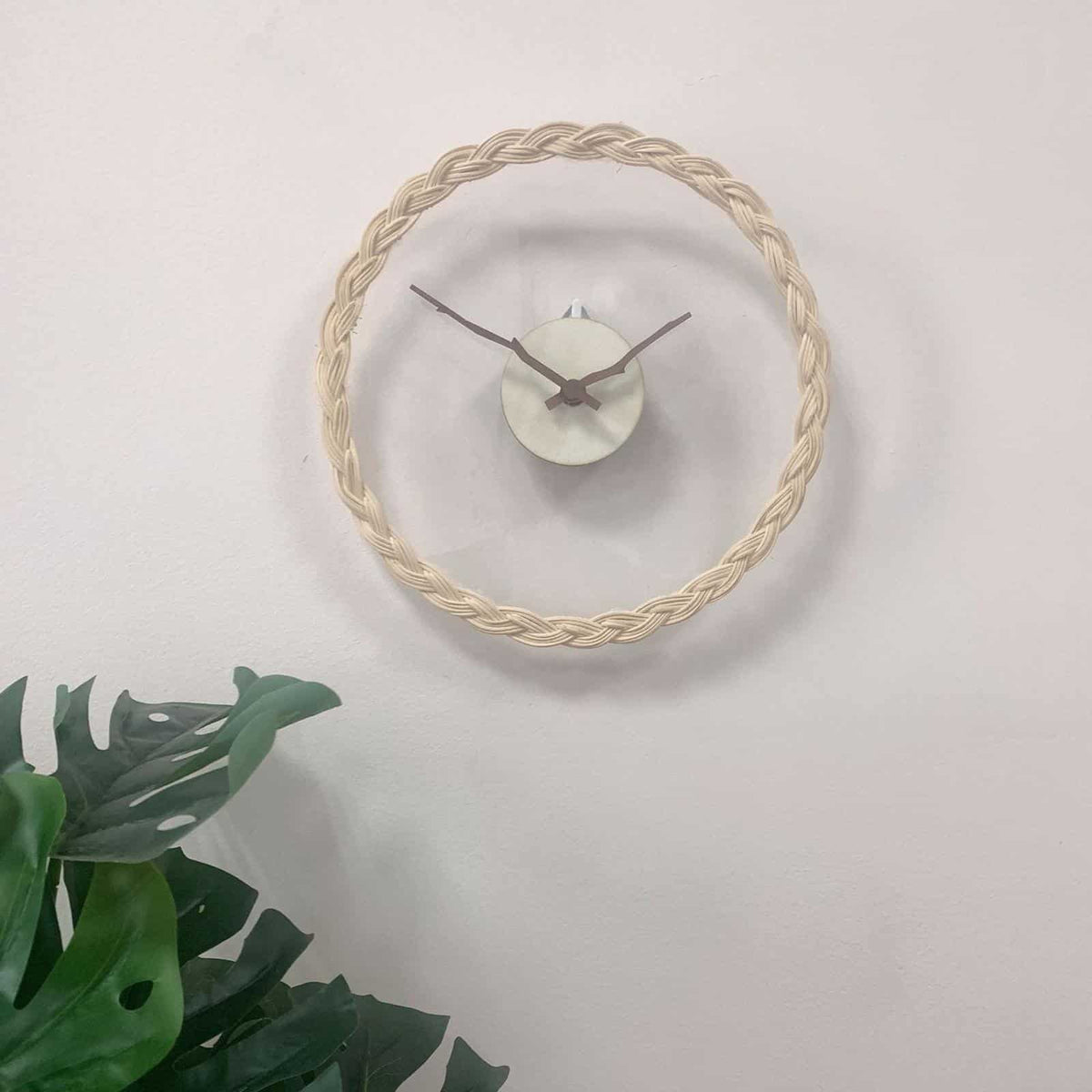Minimal rattan wall clock with branch-like rattan hands – shown in a room setting