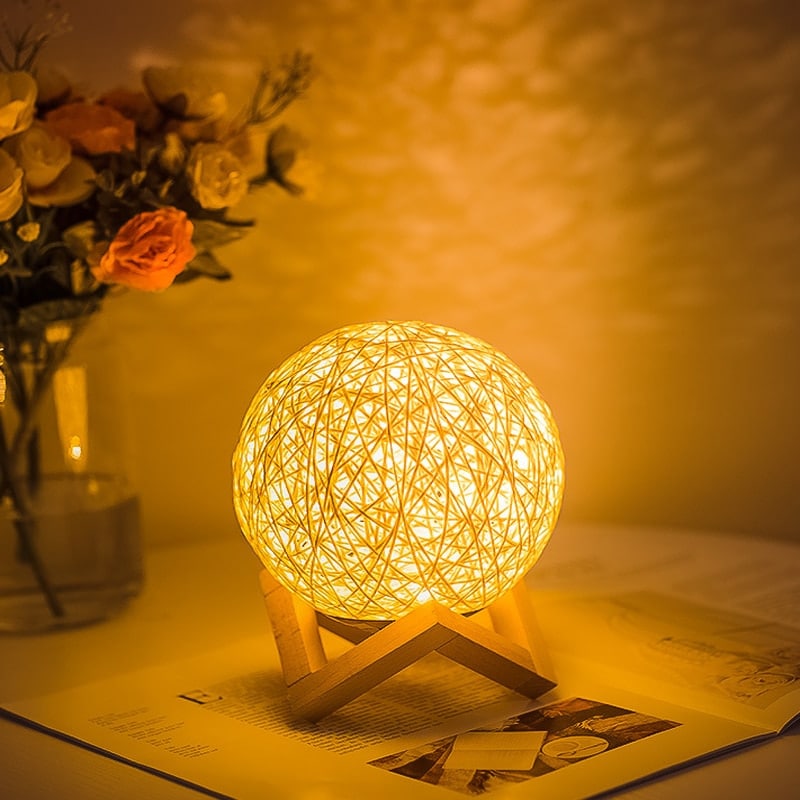 Hand-braided rattan ball LED bedside lamp – shown lit in a room setting